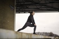 Female runner leaning forward stretching on warehouse platform — Stock Photo