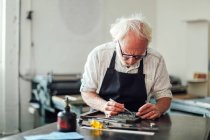 Artigiano anziano che lavora alla tipografia nel laboratorio di stampa — Foto stock