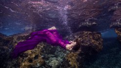 Жінка спирається назад, притягується у фіолетовій тканині, підводний вигляд — стокове фото