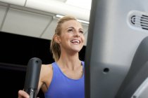 Mujer en el gimnasio usando máquina de ejercicios sonriendo - foto de stock