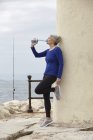 Mujer madura al aire libre, apoyada en la pared, bebiendo de la botella de agua - foto de stock