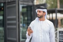 Hombre vistiendo ropa tradicional de Oriente Medio usando smartphone, Dubai, Emiratos Árabes Unidos - foto de stock