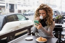 Femme dans un café utilisant un smartphone buvant café, Milan, Italie — Photo de stock