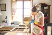 Jovem mulher derramando sabão de lavanda líquido em moldes em oficina de sabão artesanal — Fotografia de Stock