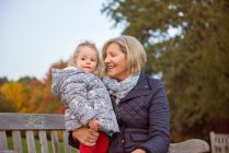 Seniorin sitzt mit Kleinkind-Enkelin im Herbstpark — Stockfoto