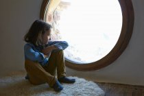 Girl sitting on floor gazing through circular window — Stock Photo
