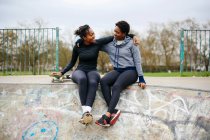 Two young female skateboarding friends sitting in skateboard park — Stock Photo