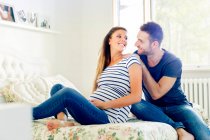Schwangere sitzt lächelnd auf Bett — Stockfoto