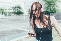 Retrato de mujer joven escuchando auriculares y bailando fuera del edificio de oficinas - foto de stock