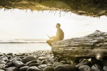 Мужчина сидит с ноутбуком и смотрит с пляжа в Провинциальном парке Хуан-де-Фука, остров Ванкувер, Британская Колумбия, Канада — стоковое фото