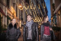 Low angle front view of friends walking down street in the evening smiling — Stock Photo