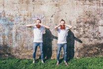 Retrato de jovens gêmeos hipster masculinos com barbas vermelhas em pé na frente da parede com as mãos cobrindo a boca e as orelhas — Fotografia de Stock