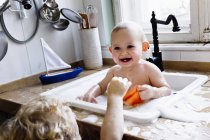 Хлопчик грає з маленьким братом, який купається в кухонній раковині — стокове фото