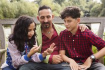 Father sitting on bench with son and daughter, daughter counting on fingers — Stock Photo