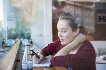 Junge Frau sitzt im Café und schreibt in Notizblock — Stockfoto
