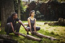 Woman with personal trainer crouching to lift tree trunk in park — Stock Photo