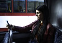 Молодая женщина сидит в автобусе, смотрит на смартфон — стоковое фото