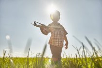 Boy in sunlit field playing with toy airplane — Stock Photo