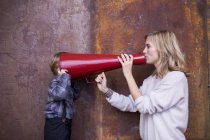 Woman speaking into megaphone, young boy listening, head in megaphone — Stock Photo