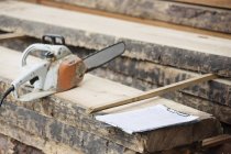 Electric saw and clipboard placed on wooden plank — Stock Photo