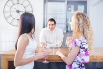 Tre giovani amici adulti che chiacchierano e bevono vino in cucina — Foto stock