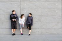 Three friends, wearing sports clothing, leaning against wall, chatting — Stock Photo