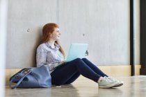 Молода студентка сидить на підлозі з ноутбуком у коледжі вищої освіти — стокове фото