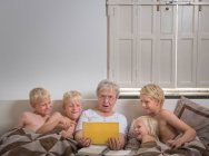 Бабуся в ліжку з онуками за допомогою цифрового планшета — стокове фото