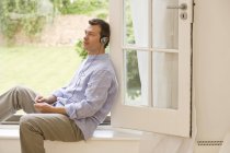 Mature man listening to headphone music at patio door — Stock Photo