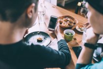 Sopra la spalla vista di due giovani amiche che leggono testi smartphone al tavolo della cucina — Foto stock