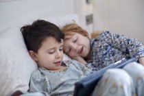 Meninos em pijama usando tablet digital na cama — Fotografia de Stock
