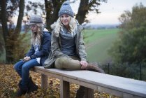 Portrait of girl and her sister sitting on autumn park bench — Stock Photo