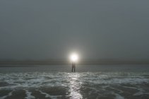 Person standing in tide, shining light out to sea — Stock Photo