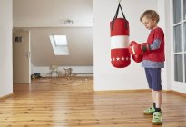Мальчик с боксерской грушей надевает боксерские перчатки — стоковое фото