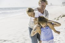 Pai ajudando filhos com piggyback na praia — Fotografia de Stock