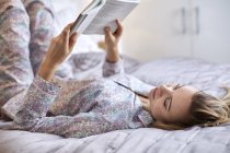 Frau im Schlafanzug liest Buch im Bett — Stockfoto