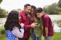 Família em pé ao ar livre, olhando para o smartphone, sorrindo — Fotografia de Stock