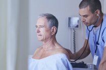 Enfermera masculina escuchando al paciente masculino mayor de nuevo con estetoscopio - foto de stock