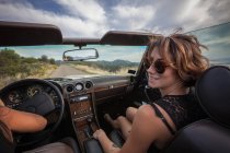 Two young women in convertible car, driving along scenic road, rear view — Stock Photo
