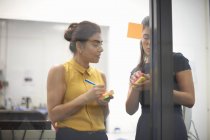 Two businesswomen writing on sticky notes for office glass wall — Stock Photo