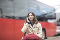 Young woman using wheelchair talking on smartphone at city bus station — Stock Photo