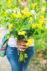 Cropped shot of woman holding bunch of fresh yellow wildflowers in garden — Stock Photo