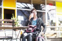 Femme en fauteuil roulant, assise à l'extérieur du café, buvant une boisson froide — Photo de stock