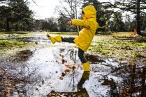 Boy in yellow anorak splashing in park puddle — Stock Photo