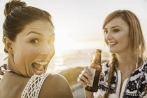 Portrait of two mid adult female friends pulling faces on beach at sunset, Cape Town, South Africa — Stock Photo