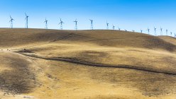 Ветряные турбины на холмах под чистым голубым небом — стоковое фото