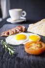 Тост с беконом, жареными яйцами и помидорами на доске — стоковое фото