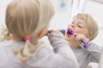 Imagem de espelho de menina loira com cachos, boca aberta escovação dentes — Fotografia de Stock