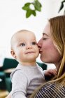 Frau trägt kleine Tochter und küsst ihre Wange — Stockfoto
