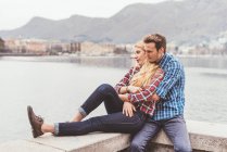 Romantique jeune couple assis sur le mur du port, Lac de Côme, Italie — Photo de stock